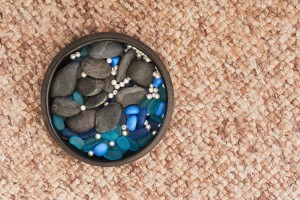Pearls and colored stones in clay vase on carpet background.